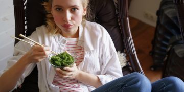 ragazza su una poltrona mentre mangia le alghe con le bacchette cinesi