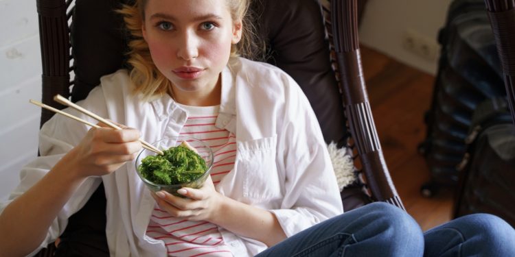 ragazza su una poltrona mentre mangia le alghe con le bacchette cinesi