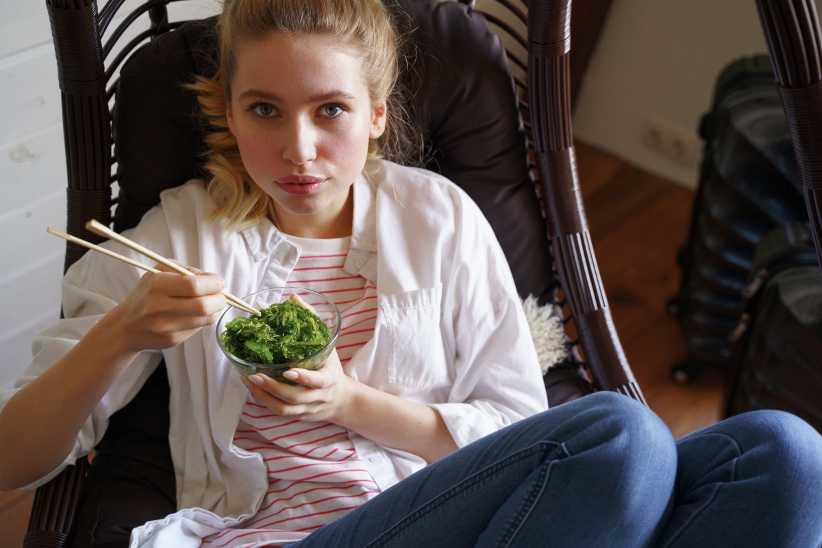 ragazza su una poltrona mentre mangia le alghe con le bacchette cinesi