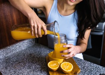 Una donna che versa in un bicchiere del succo di arancia