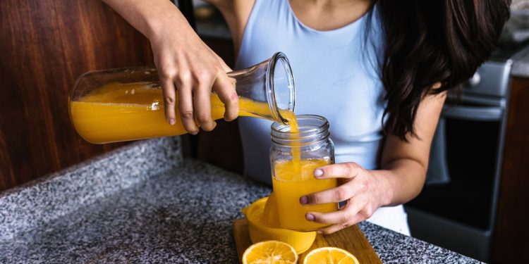 Una donna che versa in un bicchiere del succo di arancia