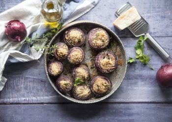 cipolle gratinate: su base di legno teglia tonda con cipolle gratinate, intorno: cipolle rosse, olio e parmigiano con grattugia