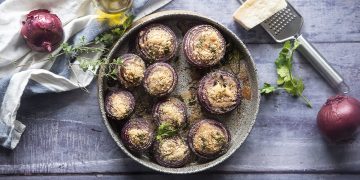 cipolle gratinate: su base di legno teglia tonda con cipolle gratinate, intorno: cipolle rosse, olio e parmigiano con grattugia