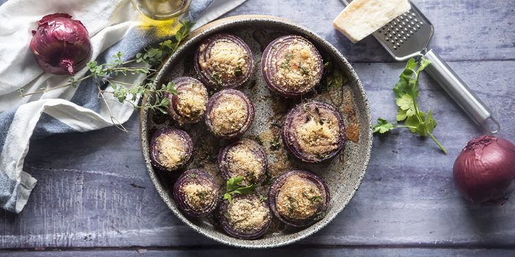 cipolle gratinate: su base di legno teglia tonda con cipolle gratinate, intorno: cipolle rosse, olio e parmigiano con grattugia