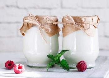 su sfondo chiaro due barattoli pieni di kefir chiusi con lo spago e tre lamponi sparsi