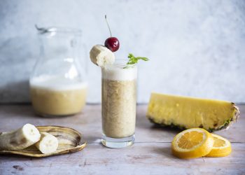 bicchiere stretto e lungo colmo di cocktail tuttifrutti analcolico, banana, ananas e fette di limone