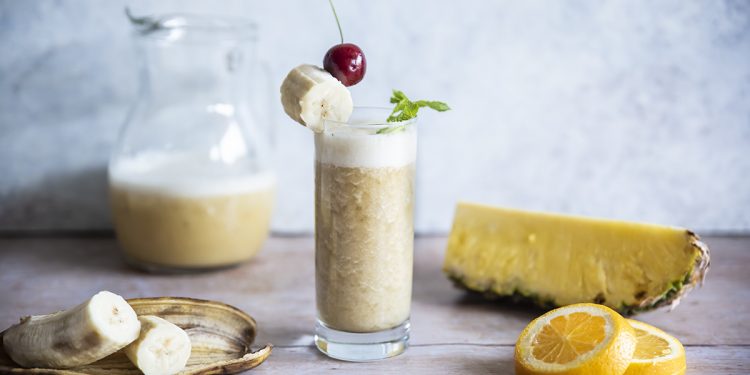 bicchiere stretto e lungo colmo di cocktail tuttifrutti analcolico, banana, ananas e fette di limone