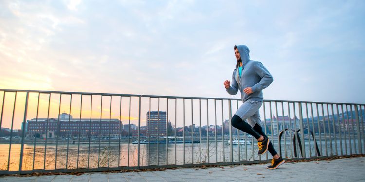 in città, un uomo corre all'alba su un ponte con una felpa con il cappuccio
