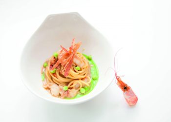 piatto fondo bianco con una porzione di spaghetti con crostacei piselli e zenzero