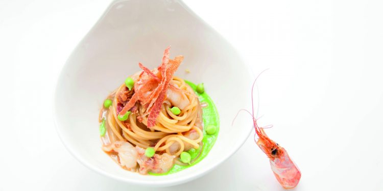 piatto fondo bianco con una porzione di spaghetti con crostacei piselli e zenzero