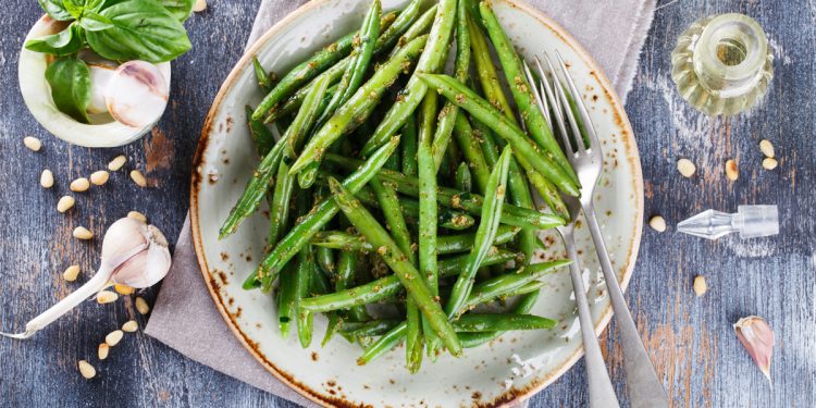 su piano azzurro apparecchiato un piatto tondo con fagiolini, accanto a spicchi di aglio e foglie di basilico