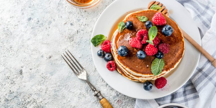 su un tavolo apparecchiato, piatto con pancake e frutti di bosco