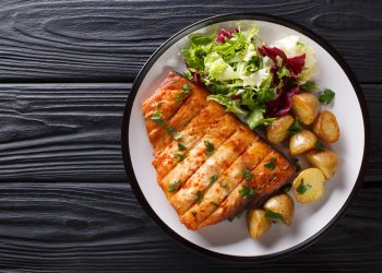 su base di legno scuro piatto tondo con trancio di pesce spada e contorno di verdure