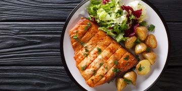 su base di legno scuro piatto tondo con trancio di pesce spada e contorno di verdure