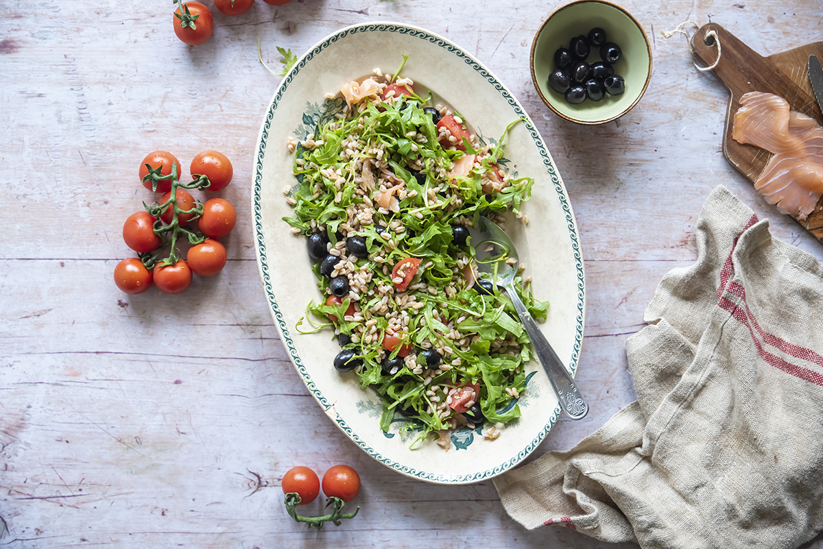piatto con insalata di farro con salmone, ciotola di olive nere, vassoio con salmone e pomodorini sparsi