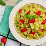 su tavolo da cucina piatto bianco con pasta alla crudaiola con pomodori e basilico, sotto tovagliolo verde e attorno pomodorini e foglie di basilico