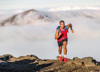 trail running: uomo in montagna con zaino e shots che corre in una gara di trail running