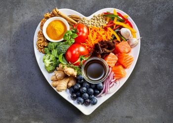un piatto a forma di cuore con dentro frutta, verdura, pesce e altri alimenti ricchi di antiossidanti naturali