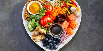 un piatto a forma di cuore con dentro frutta, verdura, pesce e altri alimenti ricchi di antiossidanti naturali
