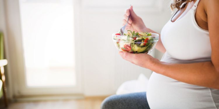 una donna incinta che mangia frutta per seguire una corretta dieta in gravidanza