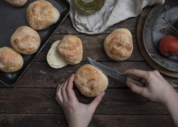 panini in una teglia e due mani che ne tagliano uno a metà