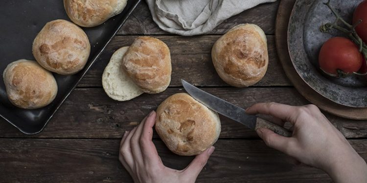 panini in una teglia e due mani che ne tagliano uno a metà