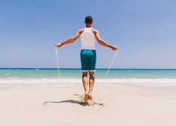 un uomo di spalle in riva al mare si allena con una corda per saltare