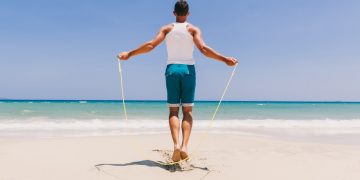 un uomo di spalle in riva al mare si allena con una corda per saltare