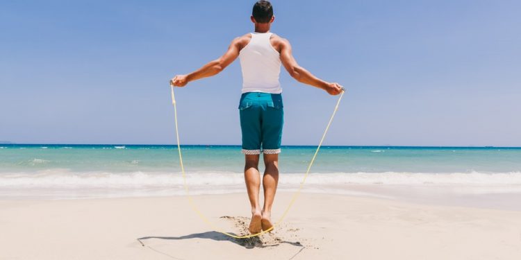 un uomo di spalle in riva al mare si allena con una corda per saltare