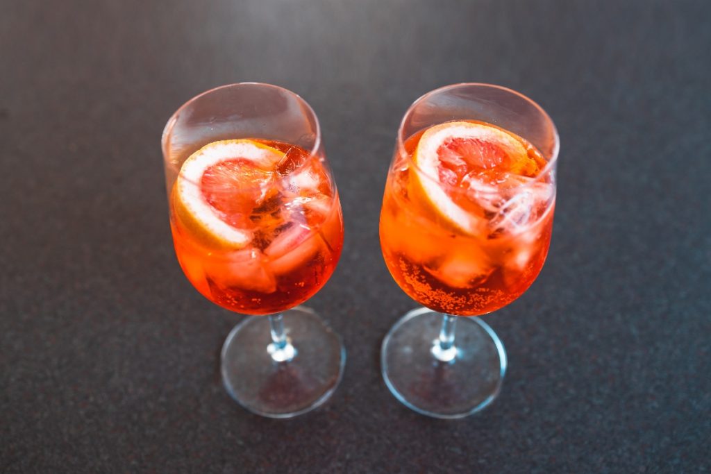 Spritz analcolico: l'aperitivo per tutti quelli che non vogliono o non possono consumare alcol 4 su base scura due bicchieri a calice pieni di cocktail Sptritz analcolico