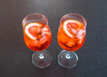 su base scura due bicchieri a calice pieni di cocktail Sptritz analcolico