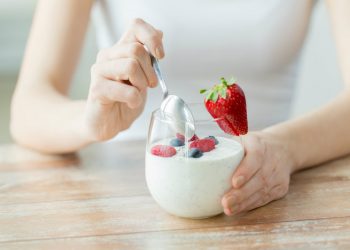 una donna che intinge il cucchiaino in un vasetto di yogurt con le fragole e frutti di bosco