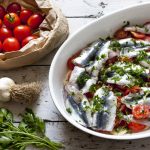 Alici alla pizzaiola: ricetta e video ricetta di questo secondo piatto veloce 1 teglia bianca ovale con tante alici alla pizzaiola, pacco di pomodorini accanto