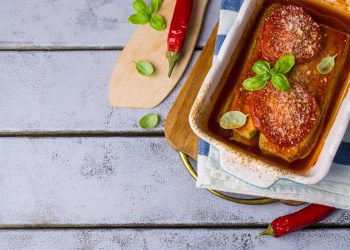 su base di legno azzurra una teglia con lasagne di tofu con parmigiana estiva