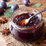in primo piano su un tavolo di legno un barattolo di vetro con la marmellata di prugne e un cucchiaino