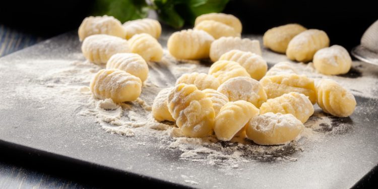 su piano da cucina: tagliere con in primo piano farina e gnocchi fatti in casa