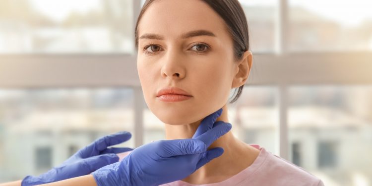 due mani con i guanti palpano la tiroide di una giovane donna