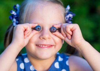 Una bambina che gioca con due mirtilli