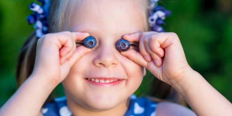 Una bambina che gioca con due mirtilli