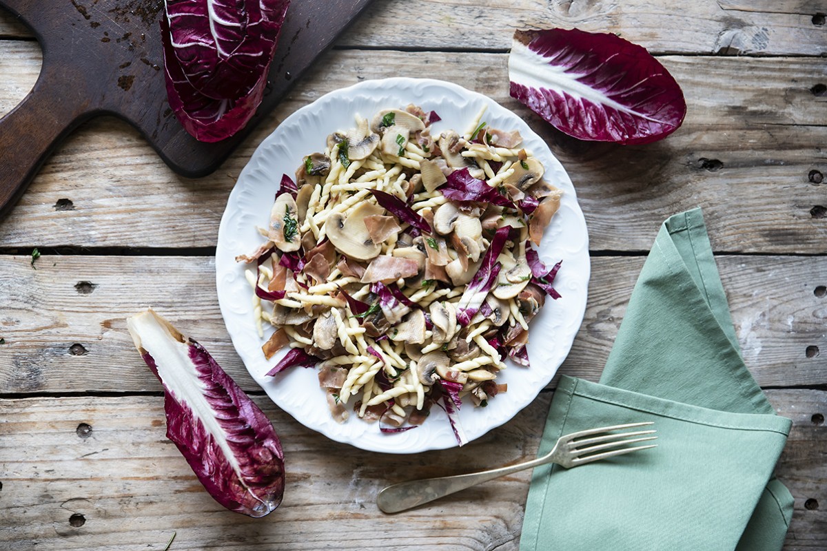 piatto bianco con pasta fredda con radicchio e funghi, foglie di radicchio intorno