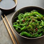 una ciotola con dentro l'alga wakame e acconto due bacchette giapponesi