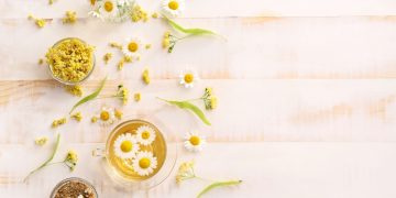 alcuni fiori di camomilla e una tazza di tisana su un tavolo