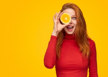 una giovane donna che tiene in mano mezza arancia perché ricca di vitamina C