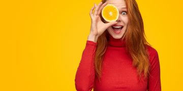 una giovane donna che tiene in mano mezza arancia perché ricca di vitamina C