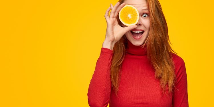 una giovane donna che tiene in mano mezza arancia perché ricca di vitamina C