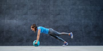 una donna in posizione di plano con una palla fitness tra le mani