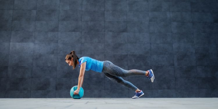 una donna in posizione di plano con una palla fitness tra le mani