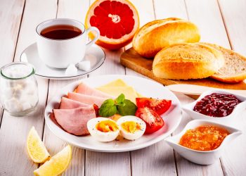 colazione proteica: un piatto con uova e prosciutto cotto, una tazza di caffè, pane, arancia e marmellate