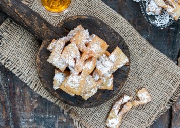 panno di iuta e sopra un vassoio di legno con manico pieno di chiacchiere al forno