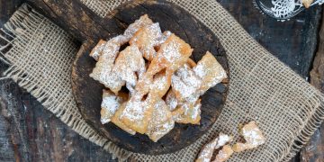 panno di iuta e sopra un vassoio di legno con manico pieno di chiacchiere al forno